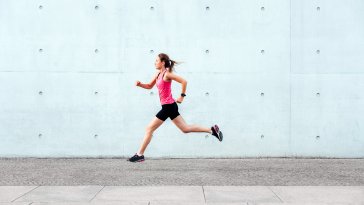 Sporty woman running in front of concrete wall 